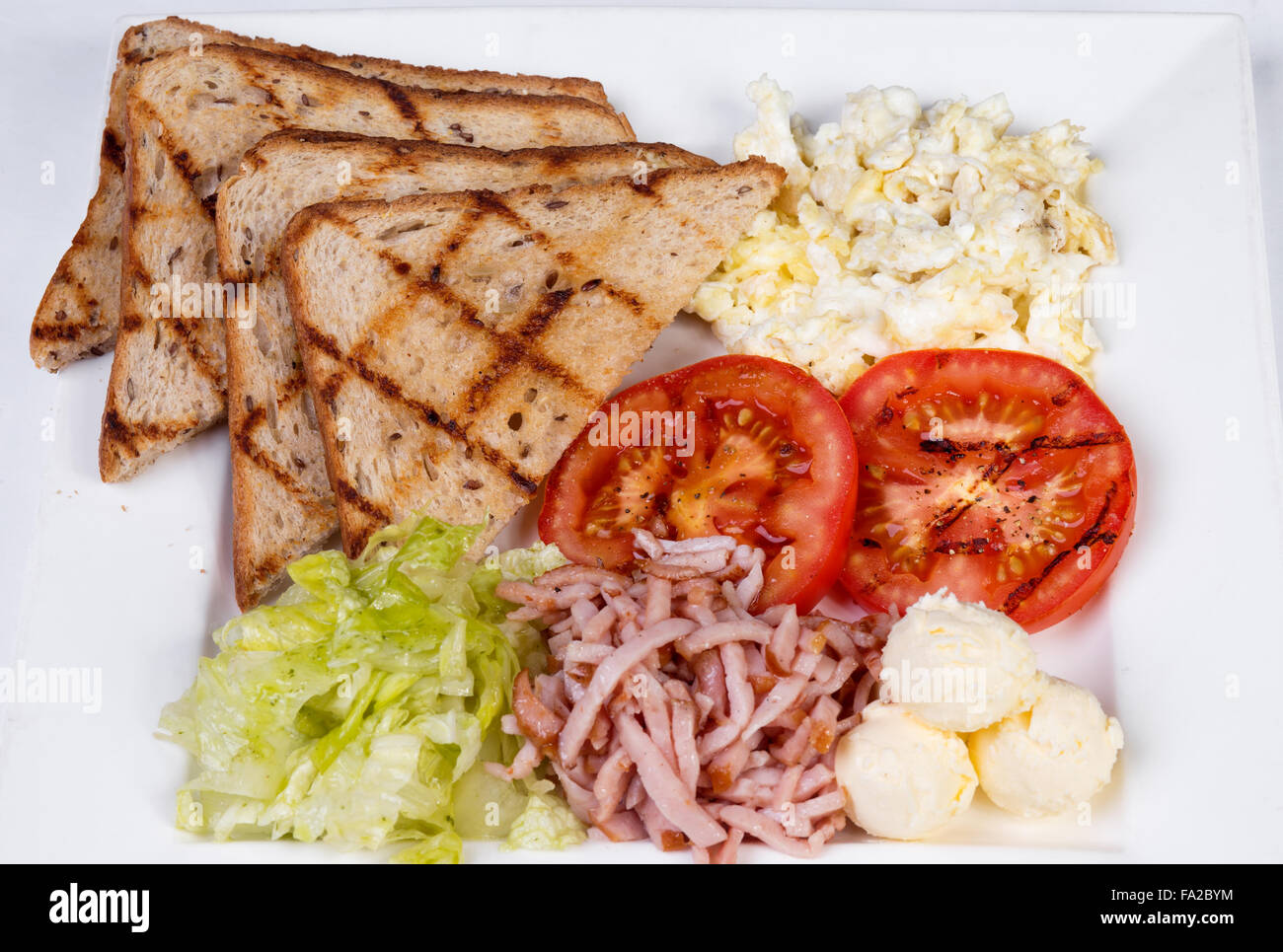 Traditional English breakfast with scrambled eggs, tomatoes, potatoes, toast and fresh salad Stock Photo