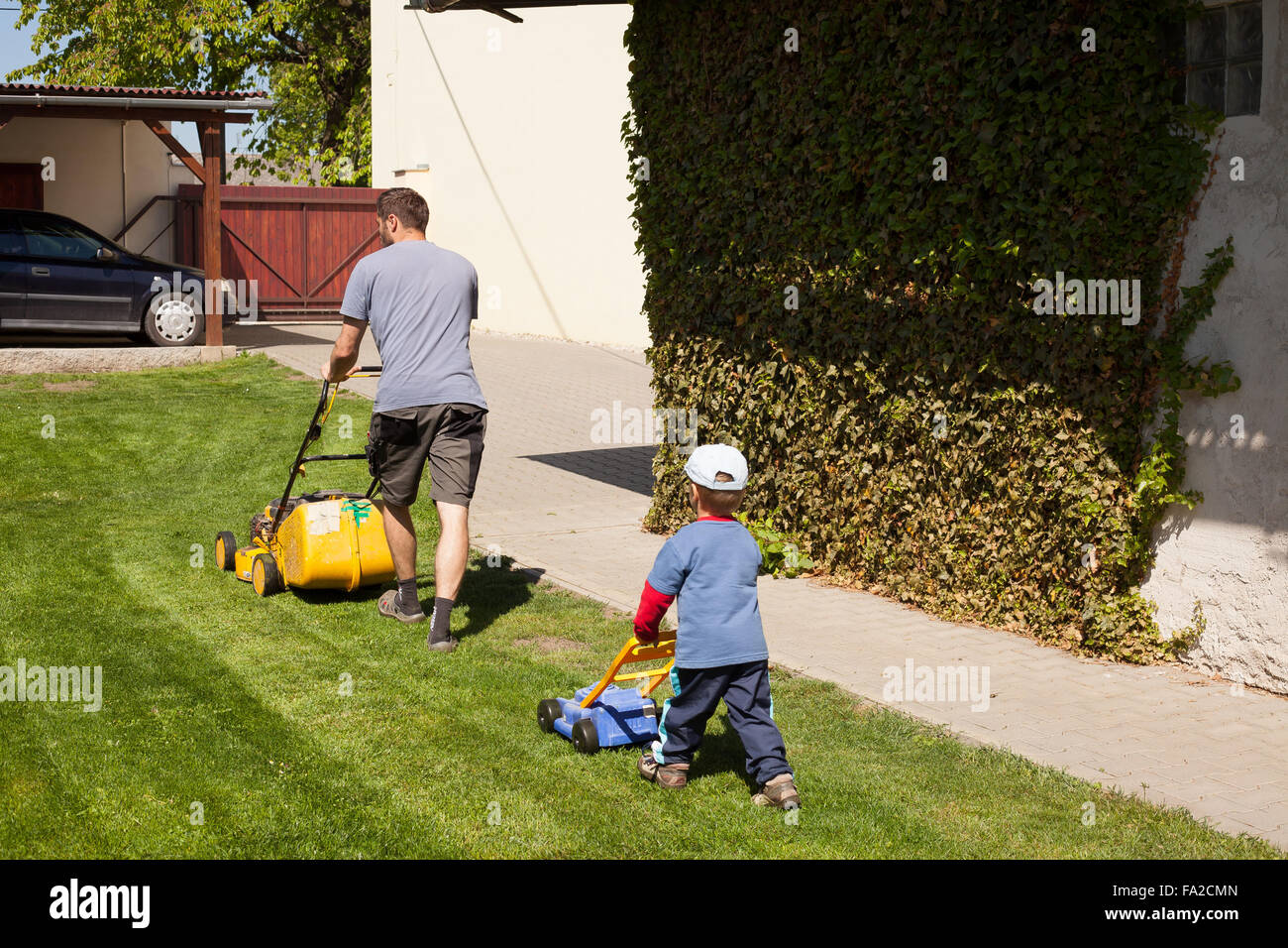 Little boy helping his father cut the grass Stock Photo - Alamy
