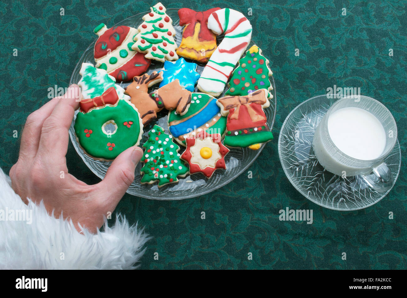 Santa Selecting A Christmas Cutout Cookie Off Of Plate, With Glass Of Milk Stock Photo