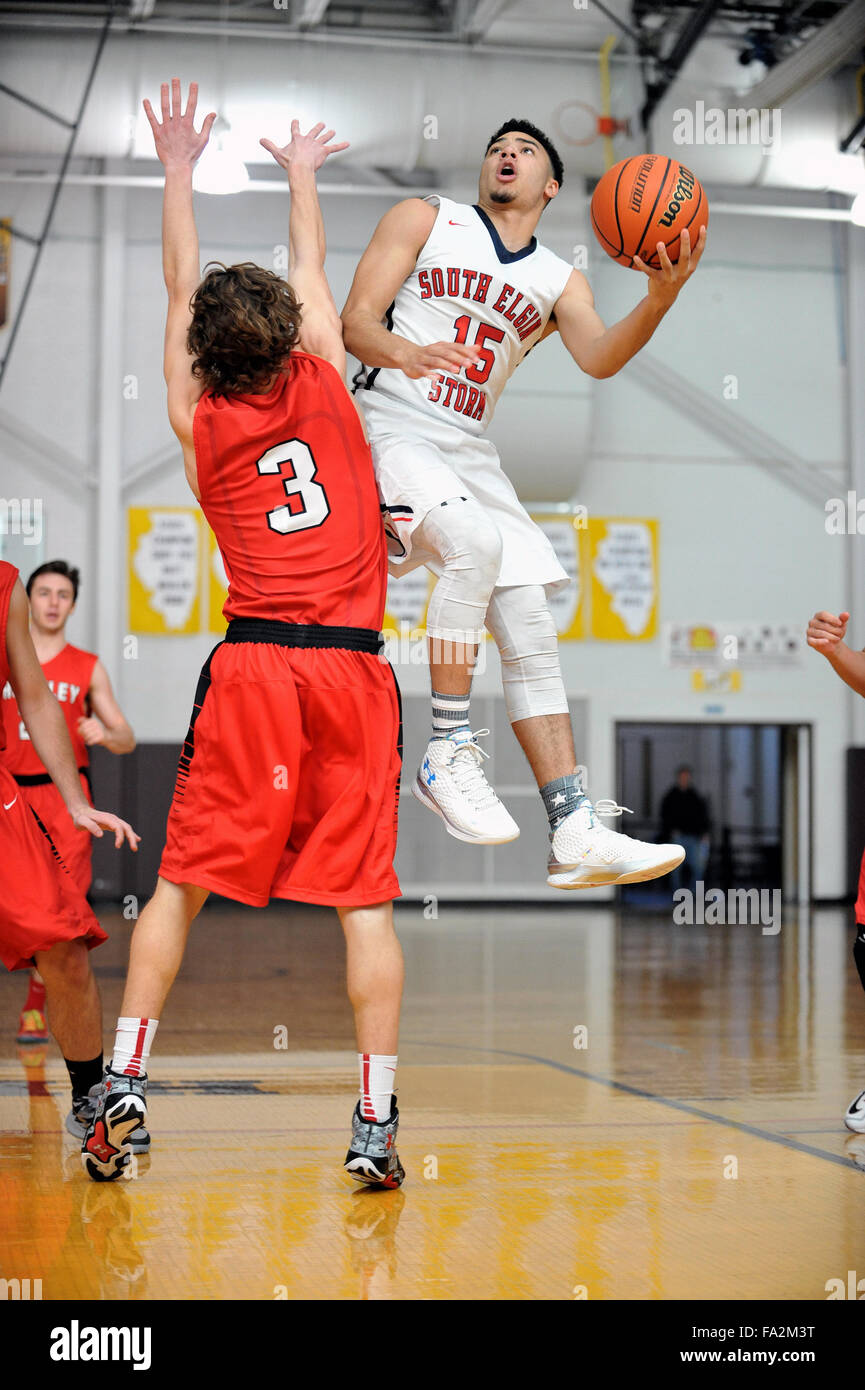 A high school guard leaves the floor and shields the ball from an opponent while finishing off a layup. USA. Stock Photo