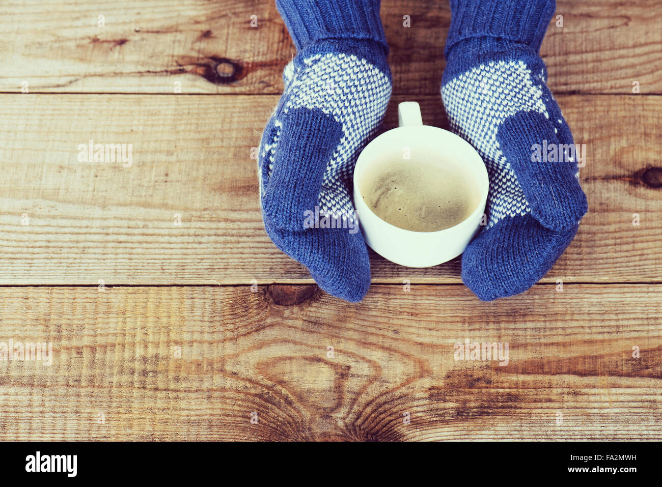 Woman hands in teal gloves are holding a mug with hot coffee or cocoa ...