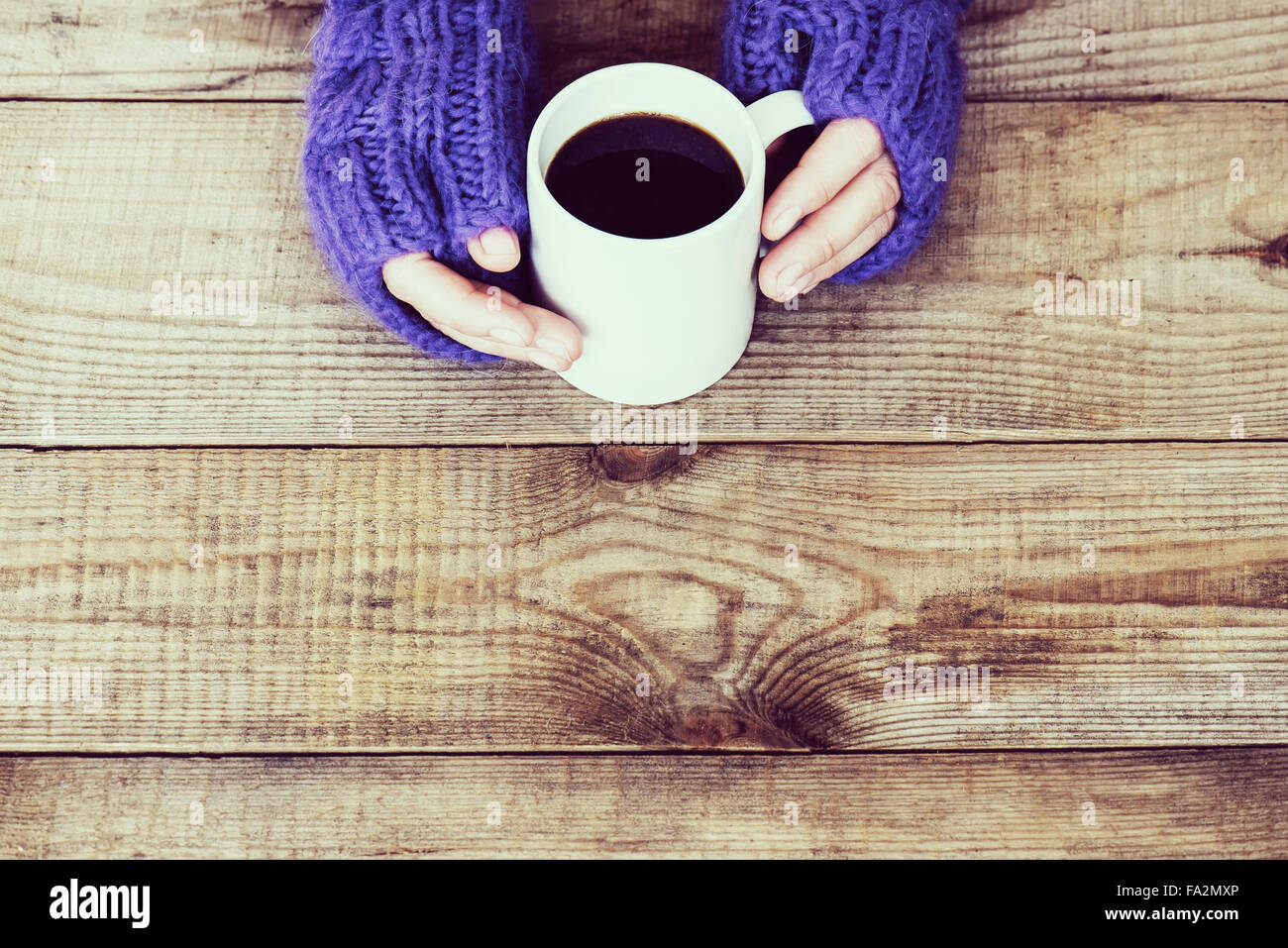 Woman hands in teal gloves are holding a mug with hot coffee or cocoa ...