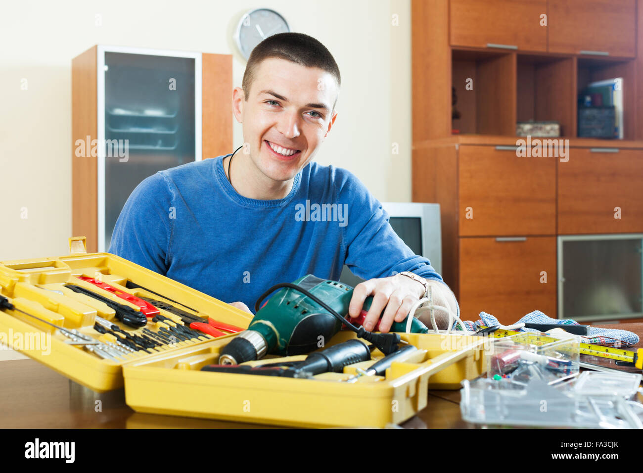 Happy smiling guy organized tools in toolbox sitting by table Stock Photo