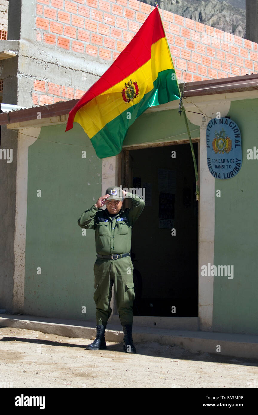 A policeman adjusts his hat under a Bolivian flag in front of the police station in Luribay, Bolivia, South America Stock Photo
