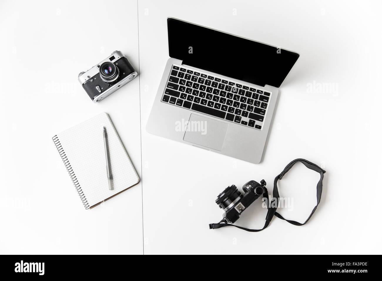 Top view of two cameras, notepad with pen and blank screen laptop