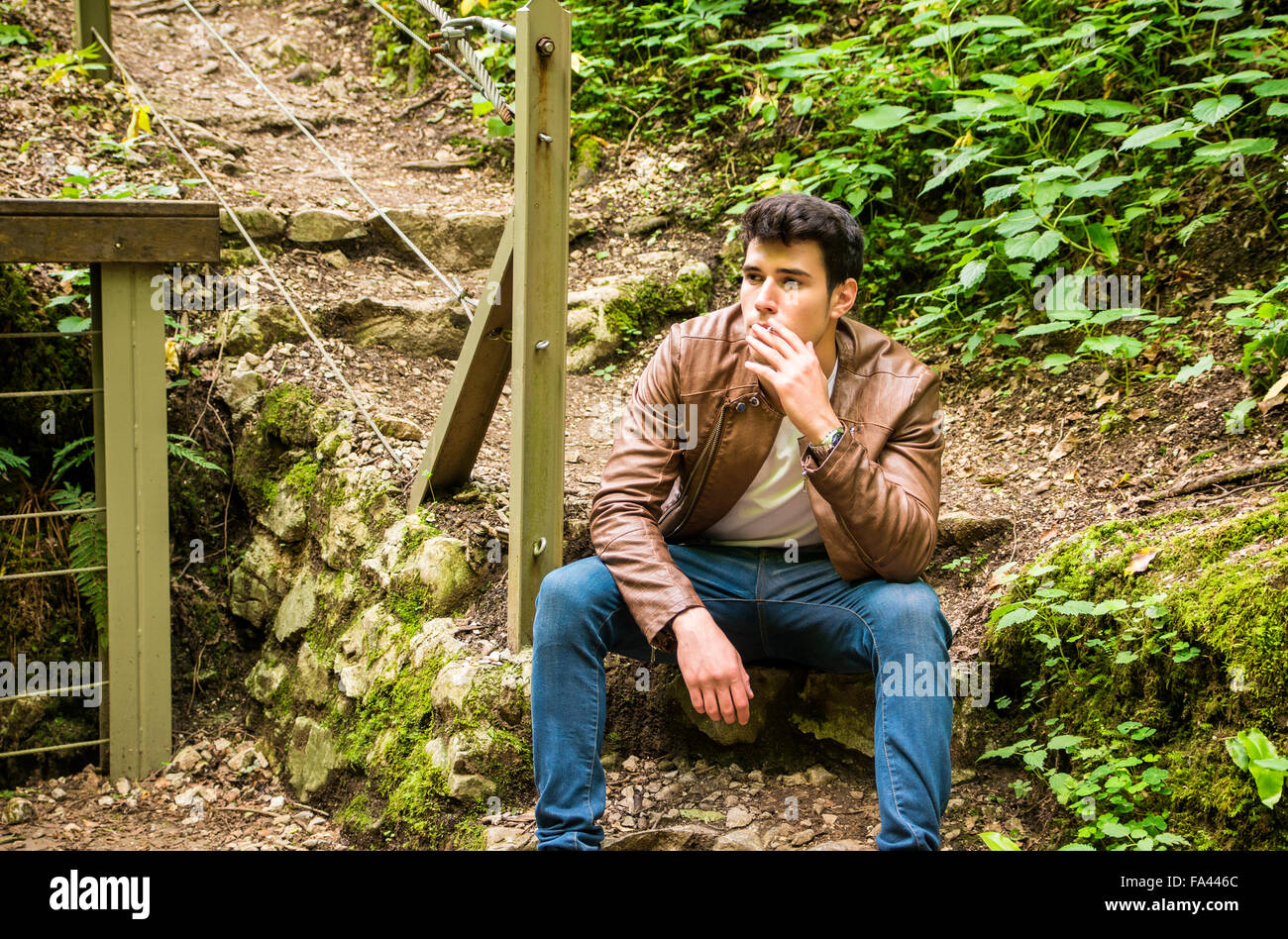 Handsome young man sitting and smoking in park, looking away Stock Photo