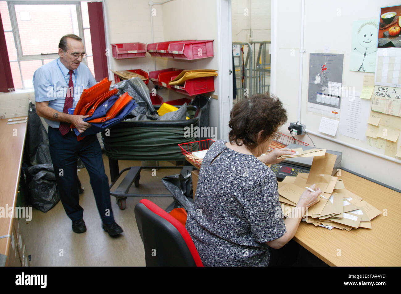 Logistic Operative unloading postal tug and external mail being processed by Clerical Officer in the Hospital post room, Stock Photo