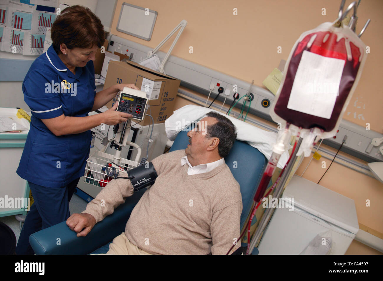 Day Care Manager taking blood pressure whilst Haematology day patient is having a blood transfusion, Stock Photo