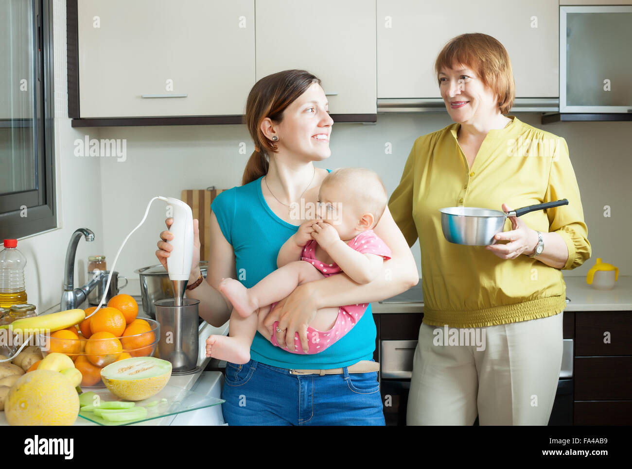 Happy family of three generations with blender cooking fruit puree in domestic kitchen at home Stock Photo