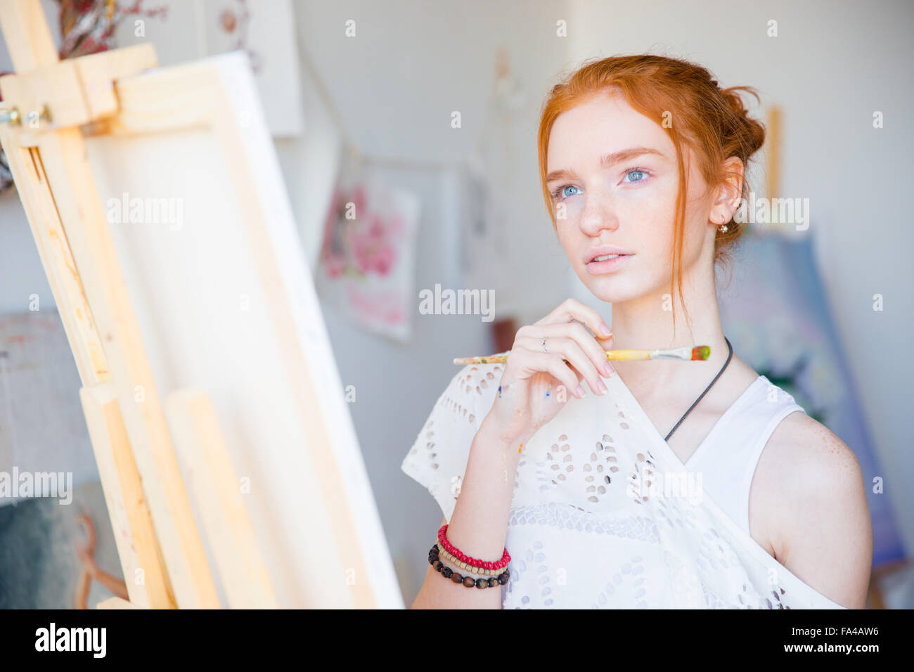 Thoughtful attractive young woman painter standing in front of easel ...
