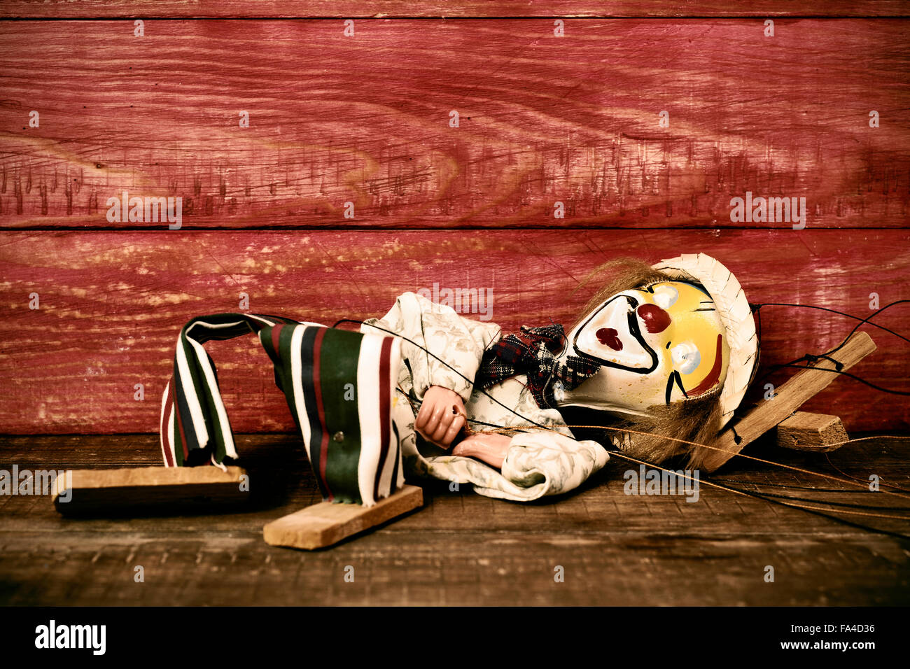 an old marionette with its face painted like a clown dropped on a rustic wooden surface, with a filter effect Stock Photo