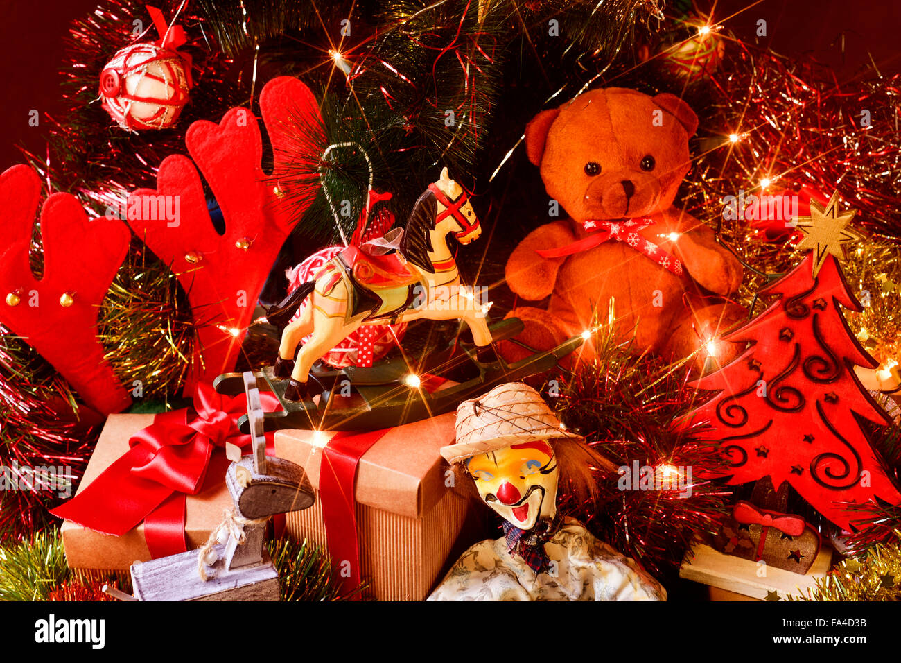 some gifts and some retro toys, such as a teddy bear, a horse or a marionette, under a christmas tree ornamented with lights, ba Stock Photo
