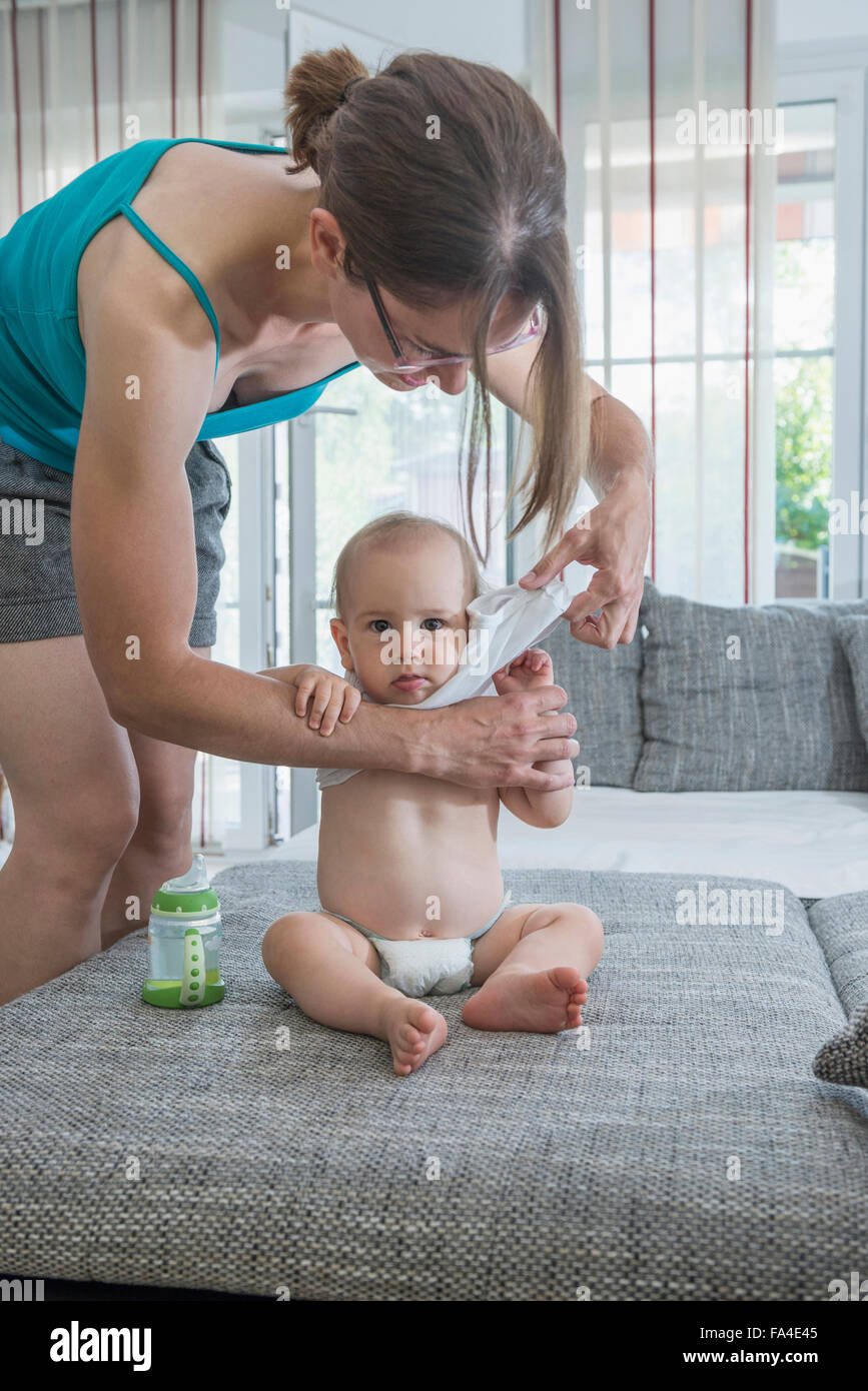 Mother changing her cute son’s clothes in bedroom, Munich, Bavaria 