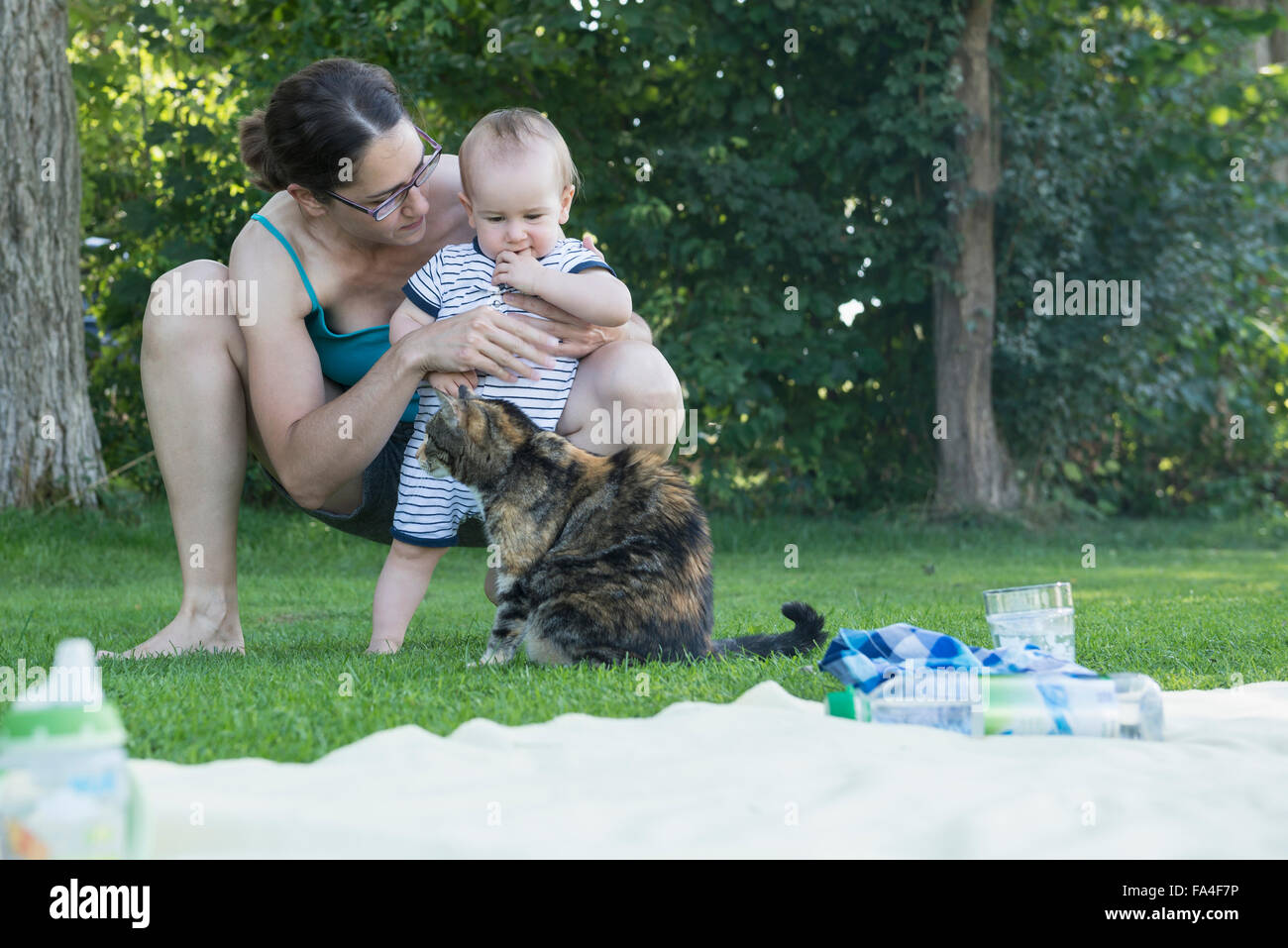 Baby boy and his mother looking at cat in lawn, Munich, Bavaria, Germany Stock Photo