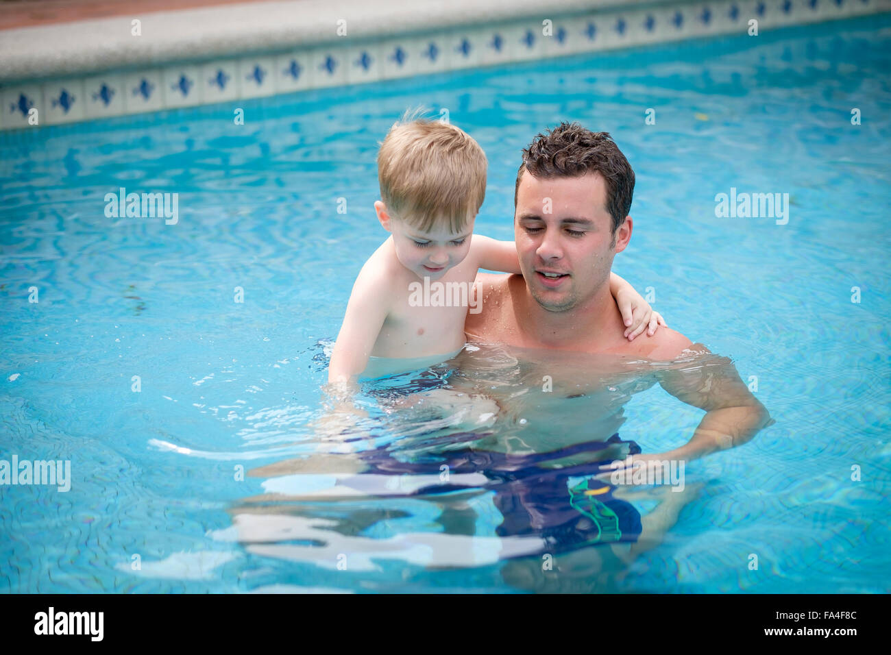 Young man carrying his toddler son in a swimming pool. Noth are enjoying the bath. Stock Photo