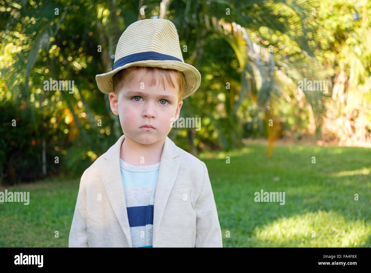 Child portrait in formal attire - Back lit portrait of toddler boy with suit jacket and hat in tropical environment Stock Photo