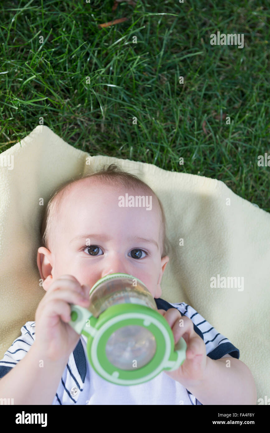 Baby boy drinking from a baby bottle lying in lawn, Munich, Bavaria