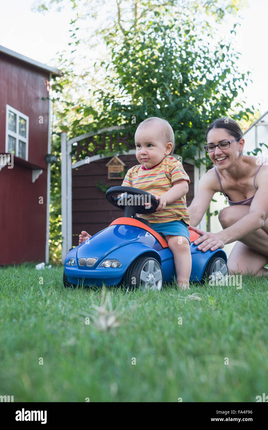 Baby boy riding on toy car with his mother pushing it from behind ...