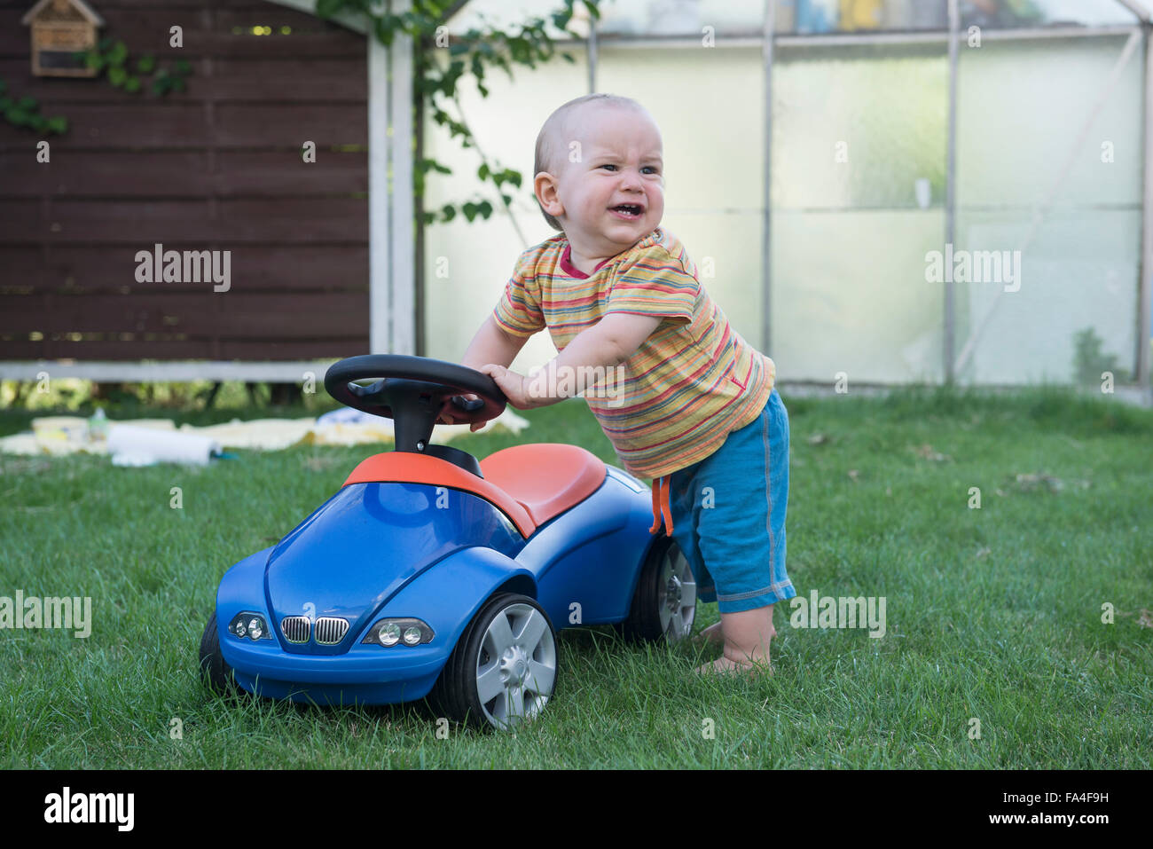 Baby boy with his toy car and crying in lawn, Munich, Bavaria, Germany Stock Photo
