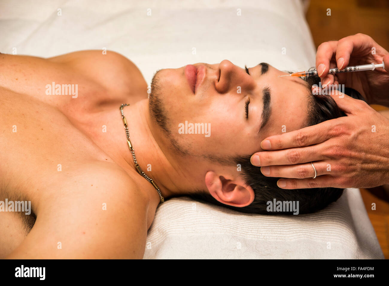 Close-up of young man getting injection of botox on forehead, laying down with eyes closed Stock Photo