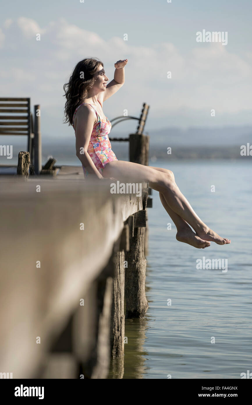 Mature woman sitting in swimsuit on pier and looking at distance, Bavaria, Germany Stock Photo