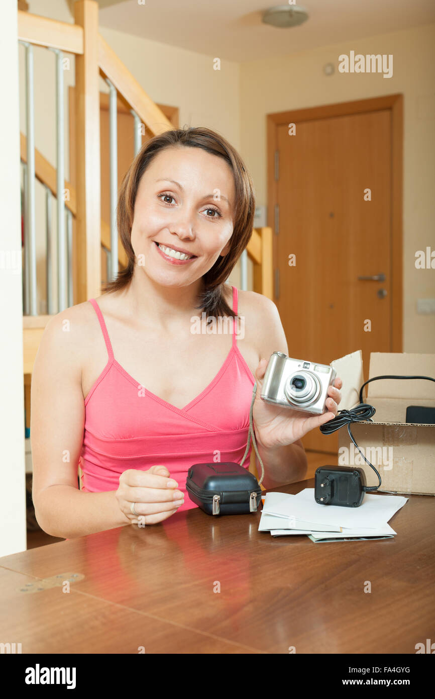 Smiling girl unpacking new compact digital camera in home interior ...