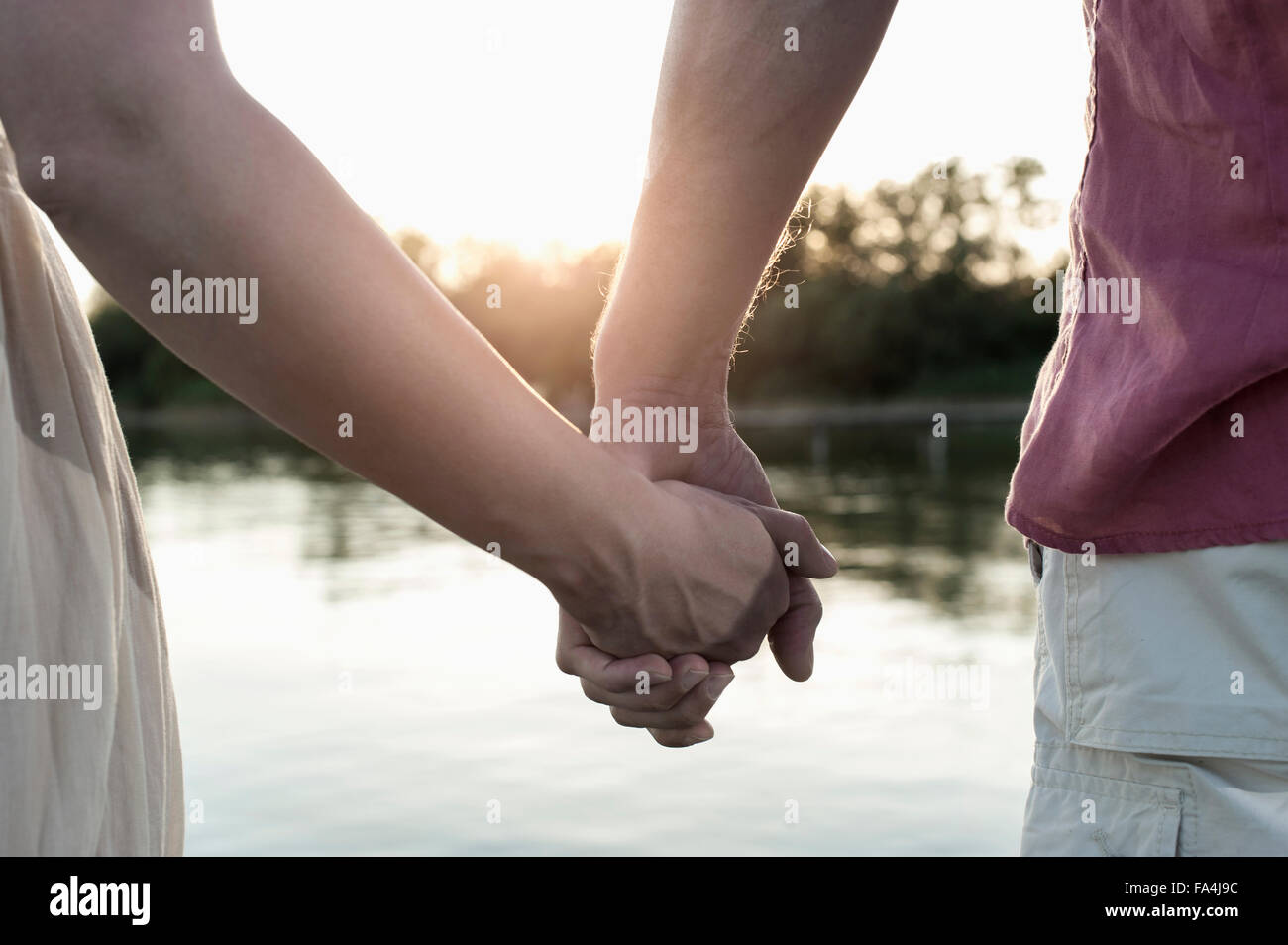 Mid section view of a couple in love holding hands during sunset ...
