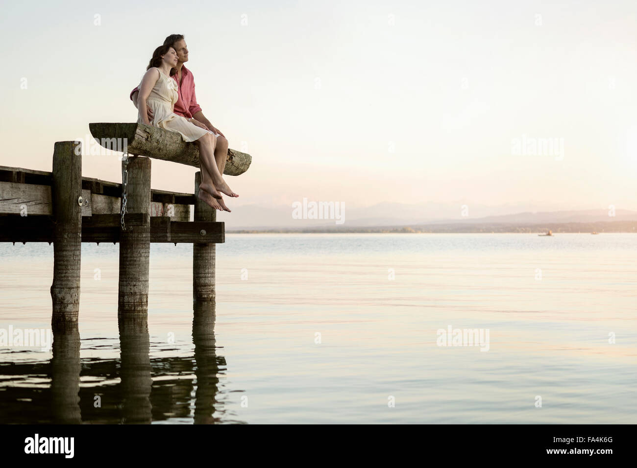 Mature couple sitting on pier looking over lake, Bavaria, Germany Stock Photo