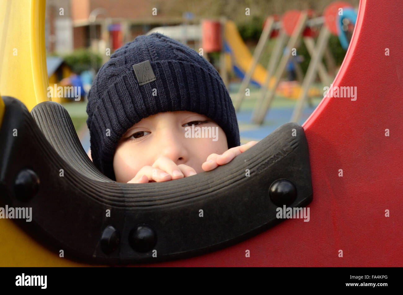 A young boy peers through a window in a climbing frame in a playground. Stock Photo