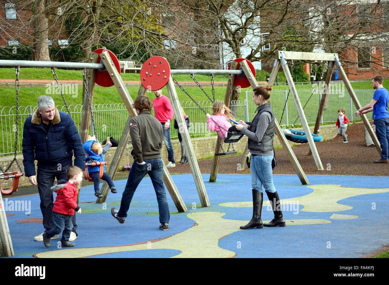 Parents and children playing on the swings in the park. Stock Photo