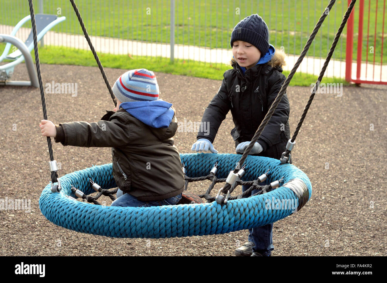 Two young boys play on a swing in a playground in Windsor Stock Photo
