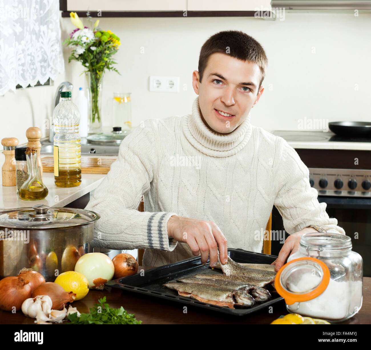smiling man putting saltwater fish into sheet pan at kitchen table ...