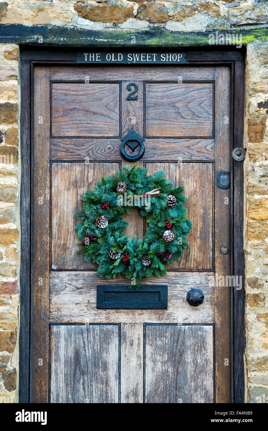 Christmas pine cone and red berry wreath on a wooden door. The old sweet shop, Kings Sutton, Northamptonshire. UK Stock Photo