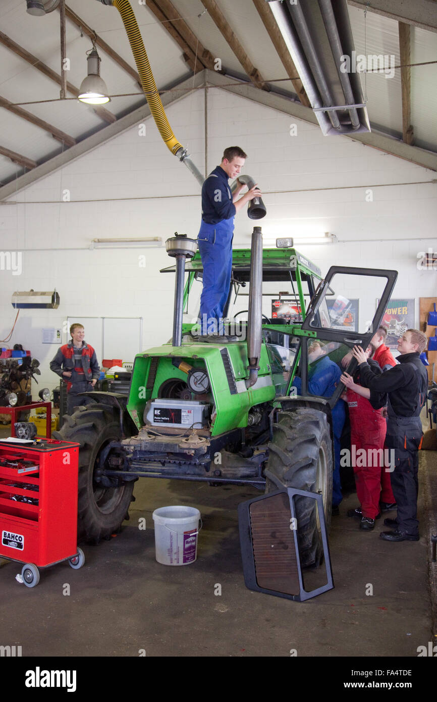 Practical education at a tractor. An apprentice attaches a waste gas suction. Stock Photo