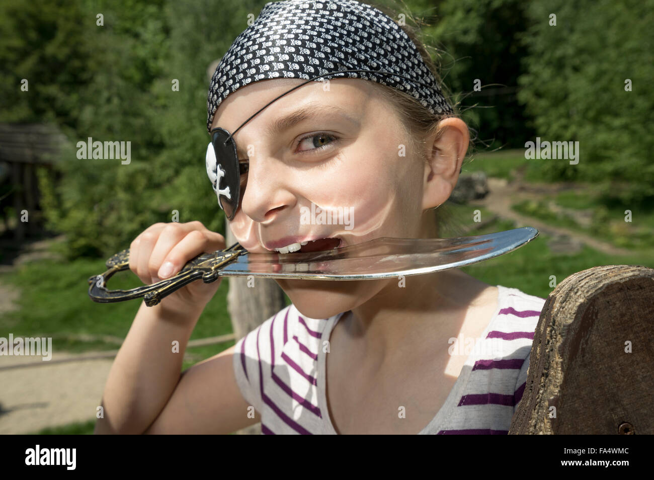 Portrait of a girl dressed up as a pirate biting saber in playground, Bavaria, Germany Stock Photo