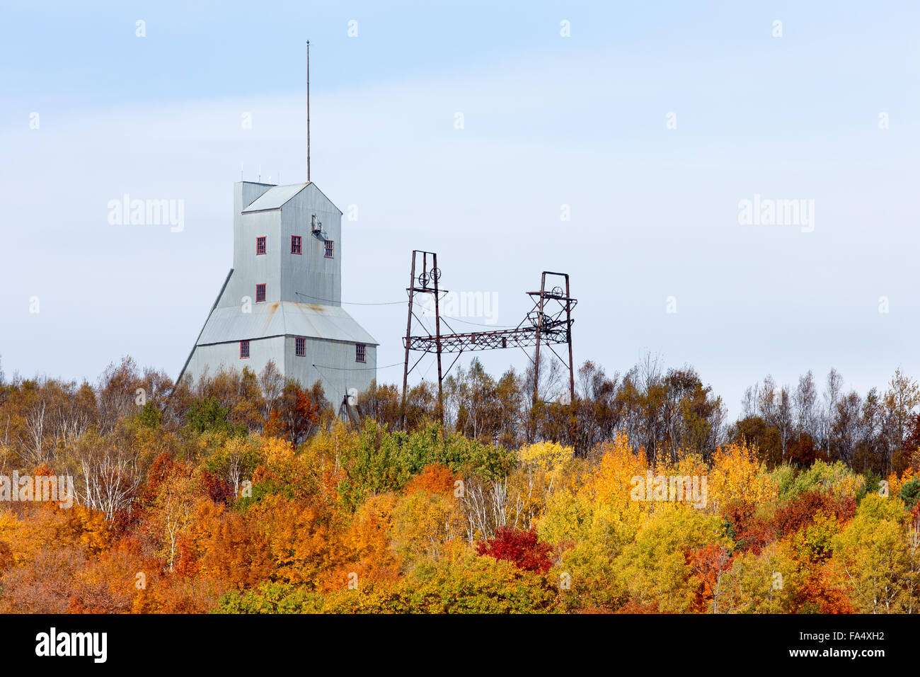 Abandoned mine shaft house and other industrial structure on a hill and behind a cluster of trees in brilliant autumn colors. Stock Photo