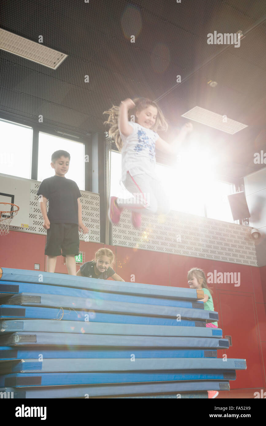 Children jumping from stack of sport mats in sports hall, Munich