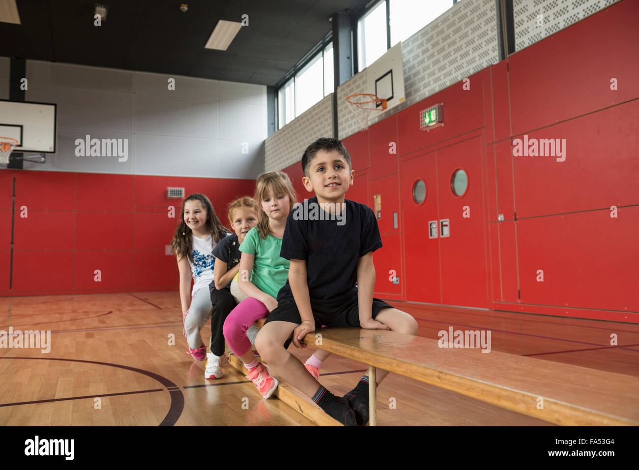 Children resting on bench before exercises in large gym of school, Bavaria, Munich, Germany Stock Photo