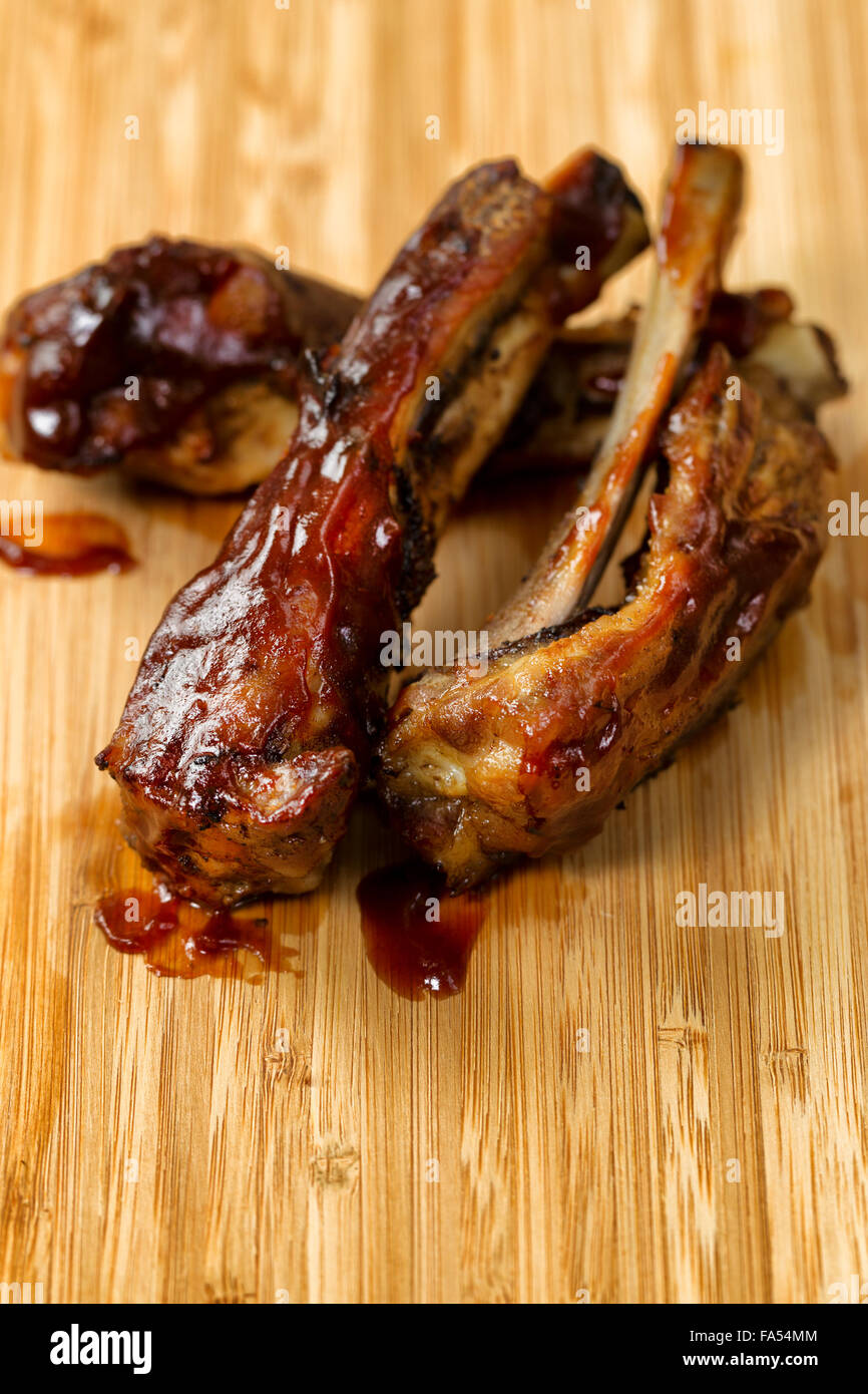 Close up of barbecued ribs with sauce on wooden cutting board. Selective focus on upper front part of ribs in vertical format. Stock Photo