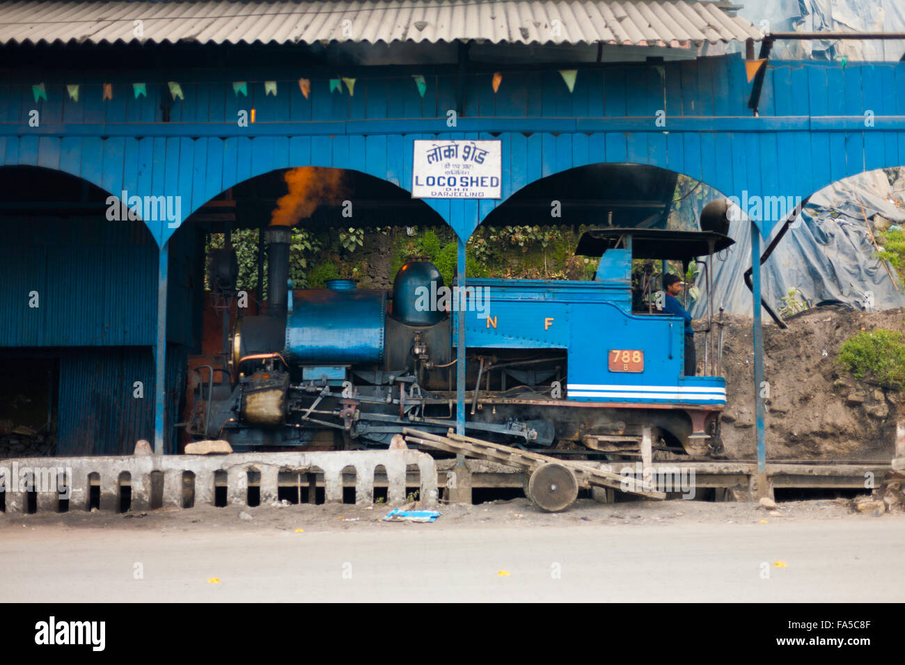 Indian driver standing inside a parked blue toy train engine in its shed Stock Photo