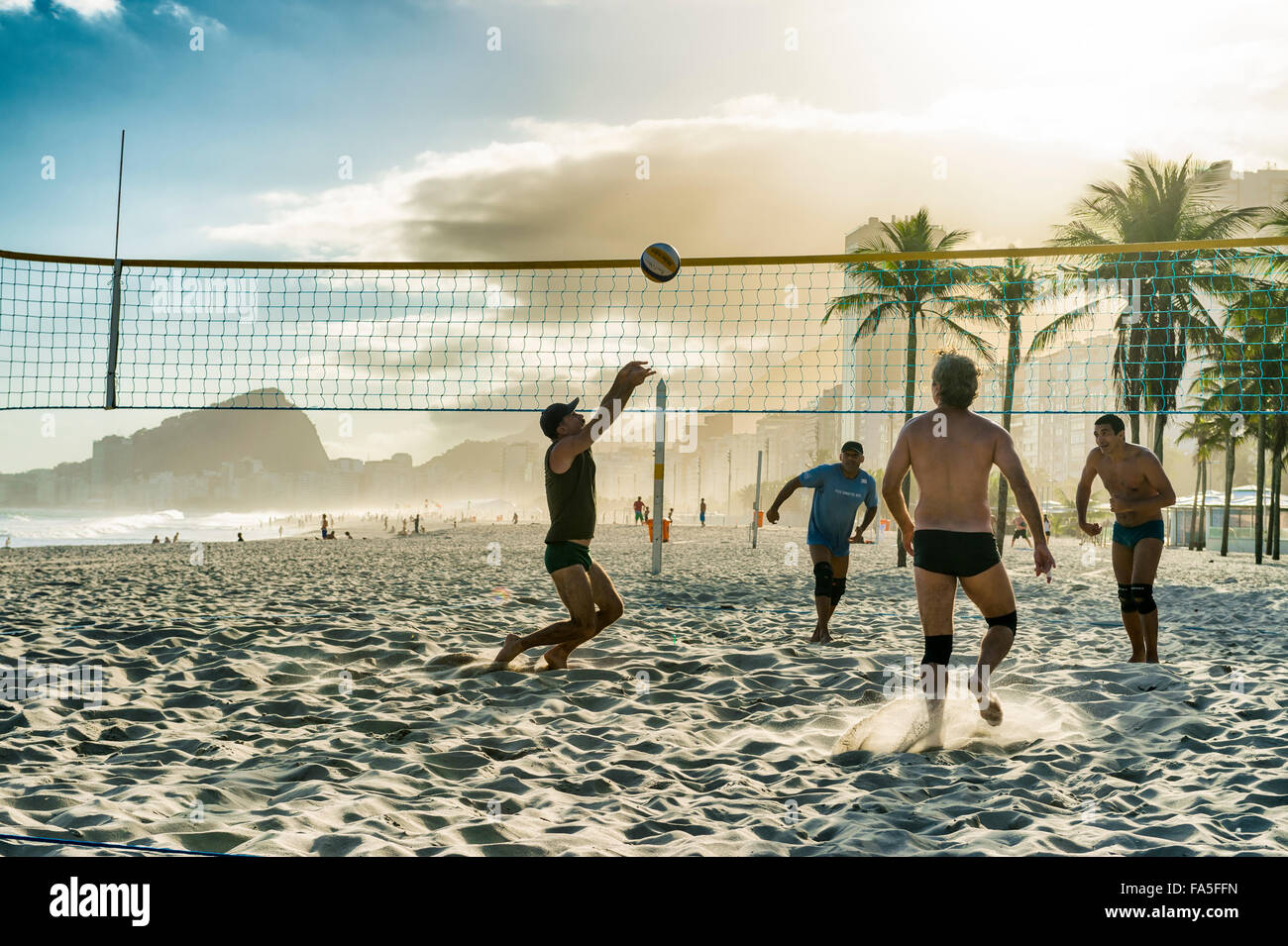 RIO DE JANEIRO, BRAZIL - OCTOBER 30, 2015: A group of young Brazilian men play volleyball at sunset at Leme Beach, Copacabana. Stock Photo