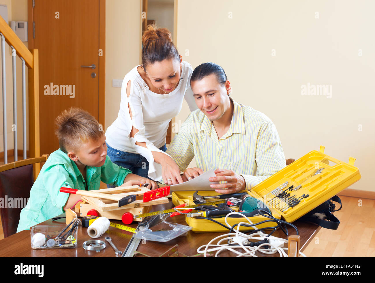 Man with son doing something with working tools, happy woman watching them in home Stock Photo