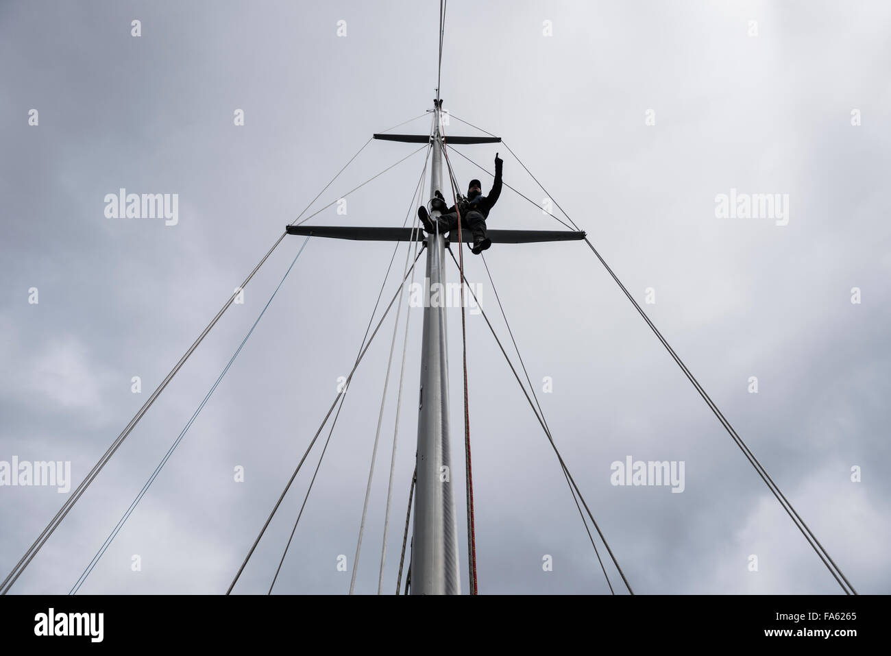 Man sitting on sailboat mast points into distance Stock Photo