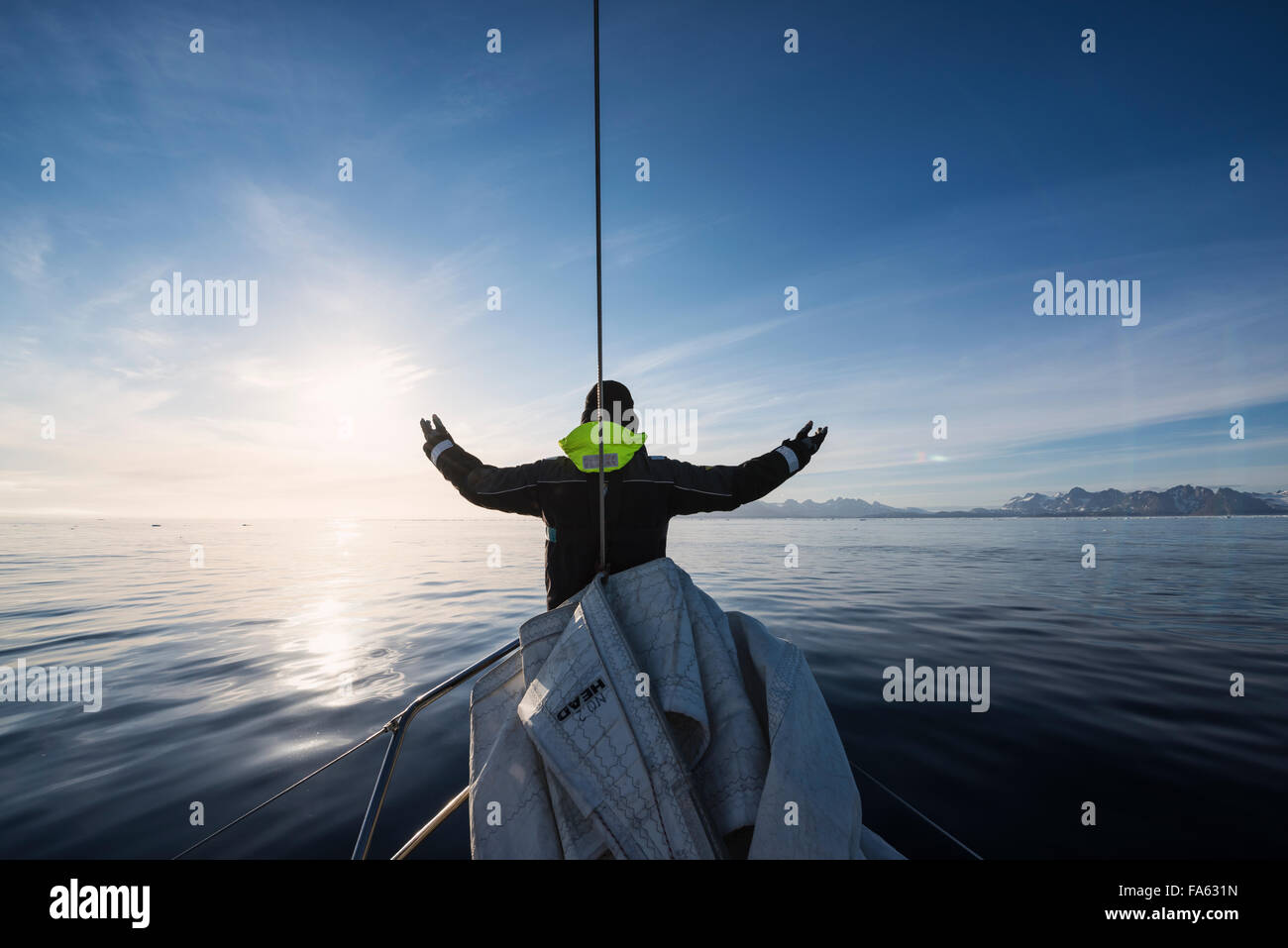 Sailor raises hands towards sun as land approaches off east coast of Greenland Stock Photo