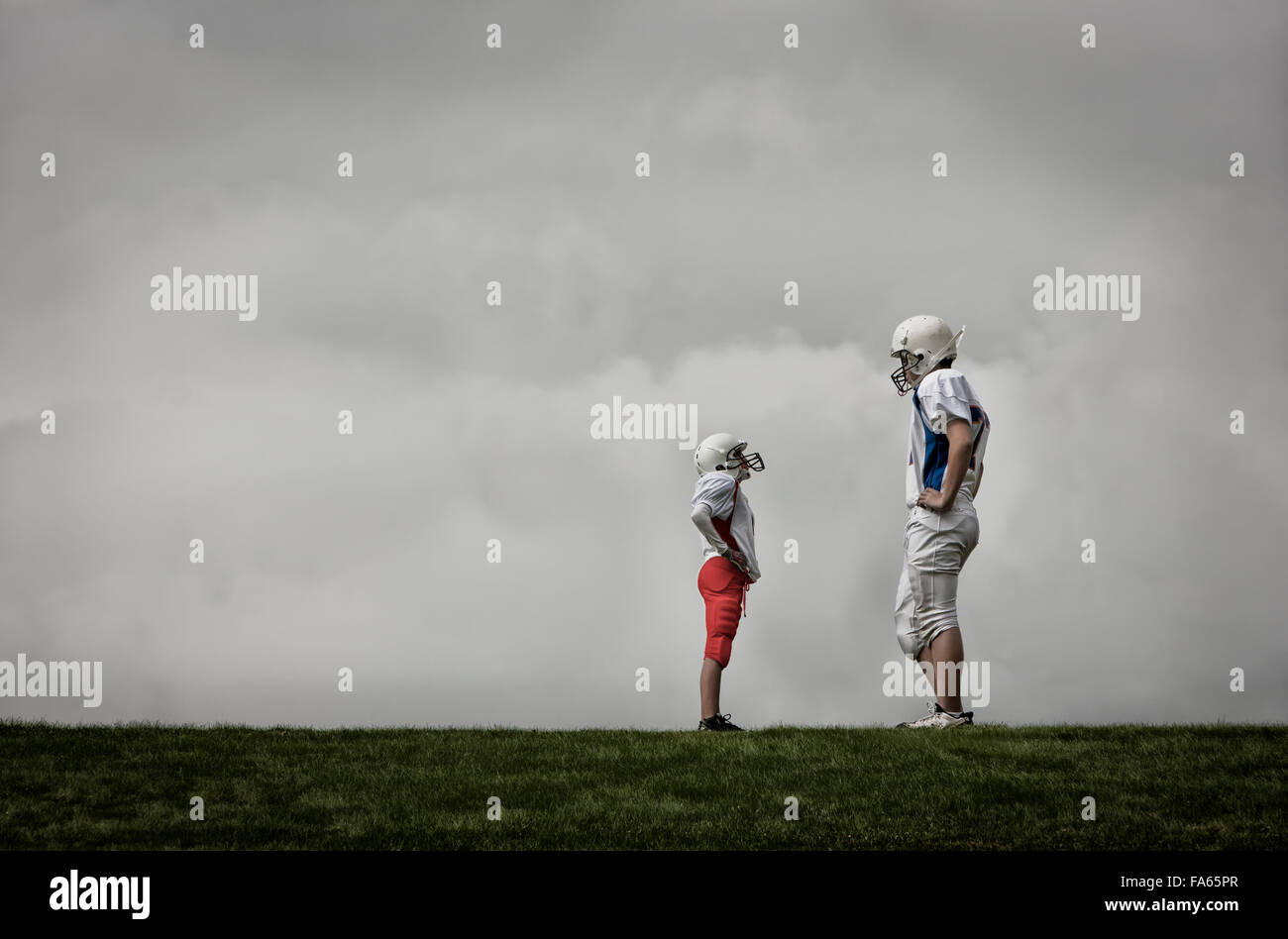 Two people facing each other, one very tall football player, and one much shorter person looking up, hands on hips. Stock Photo