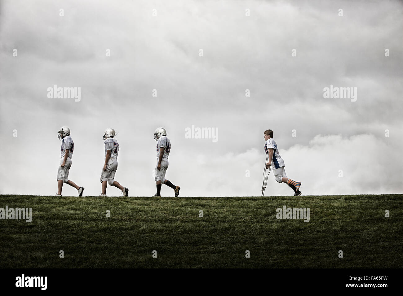 A group of football players, Three fit players walking in line, one using crutches following. Stock Photo
