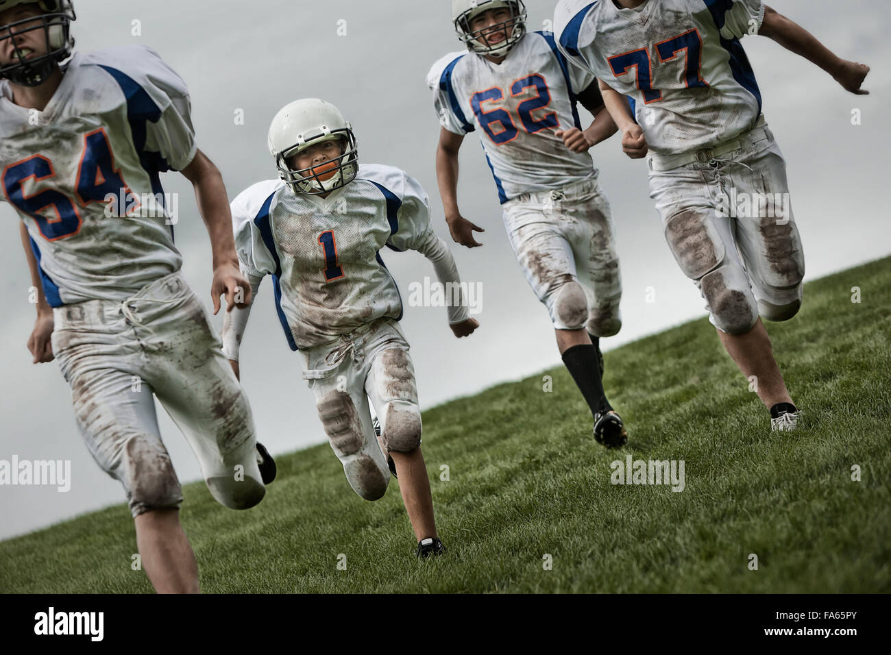 A group of four football players, young people in sports uniform and protective helmets running forward. Stock Photo