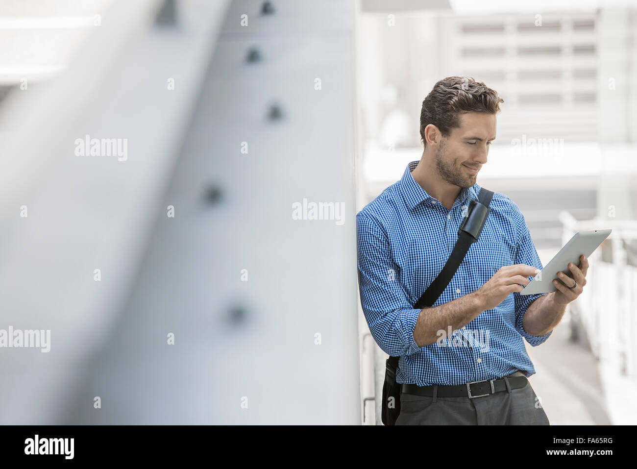 A man in shirt and tie using a handheld digital tablet in an urban scene. Stock Photo