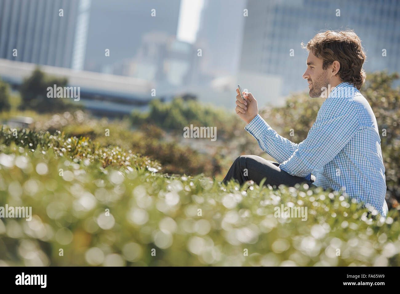 A young man on a park bench in the city, using a cell phone. Stock Photo