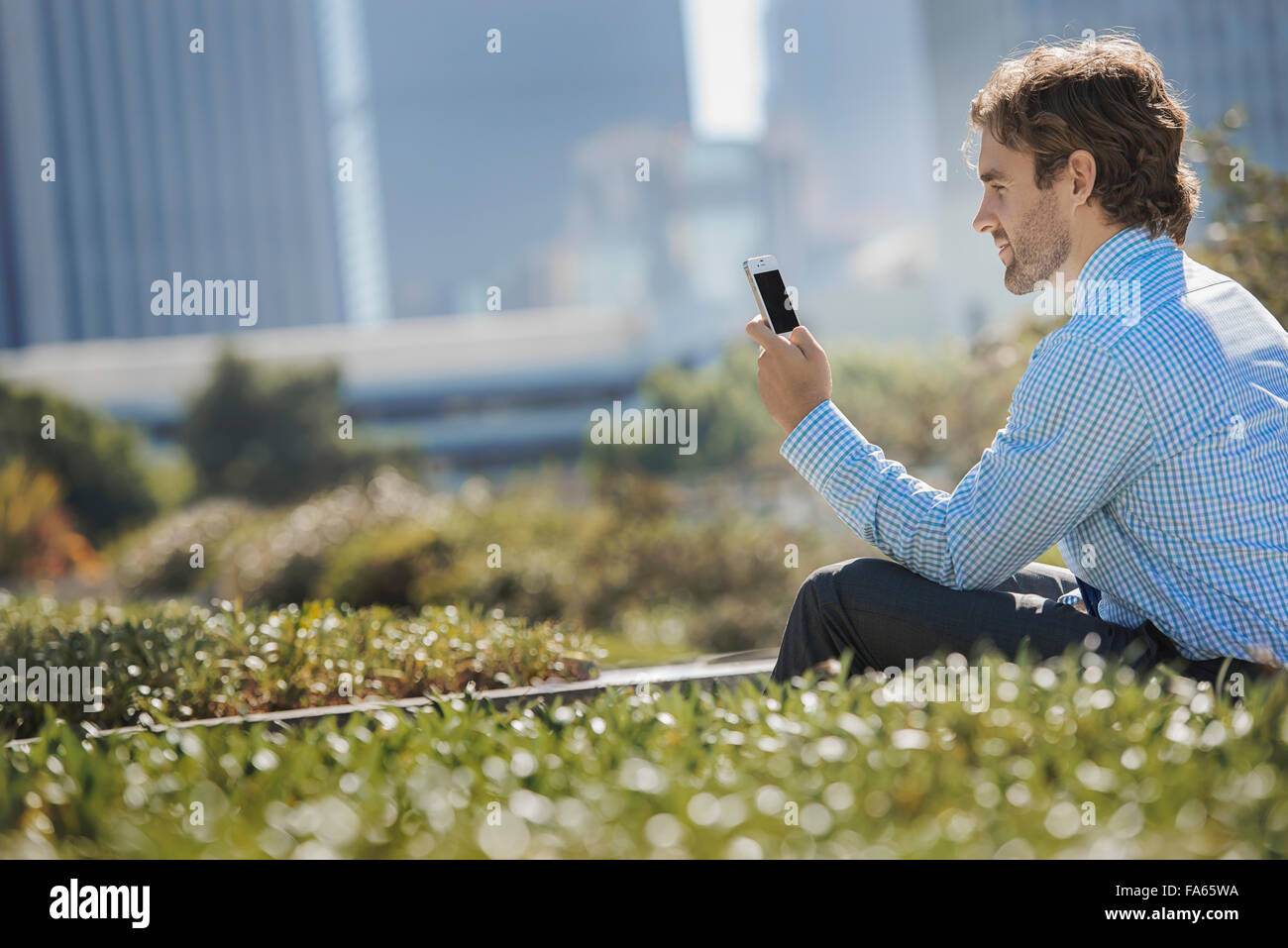 A young man on a park bench in the city, using a cell phone. Stock Photo